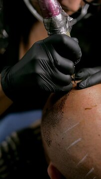 Close-up of the hands of a tattoo artist doing a hair tattoo on a man's head