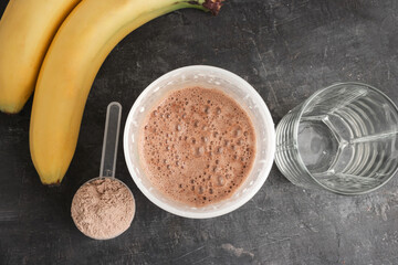 Blended chocolate protein drink in a shaker, plastic measuring spoon with protein powder, bananas...