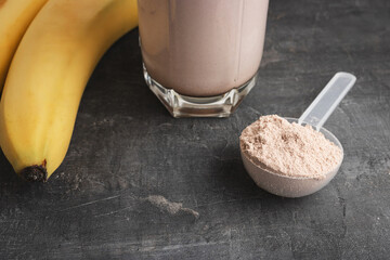 Blended chocolate protein drink in a glass with yellow straw, plastic measuring spoon with protein...