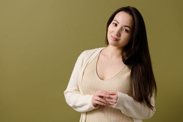 Fototapeta premium Asian woman in beige top and cardigan looking at camera isolated on green 