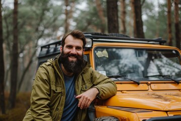 Portrait of a smiling bearded man next to his off-road car in the mountains