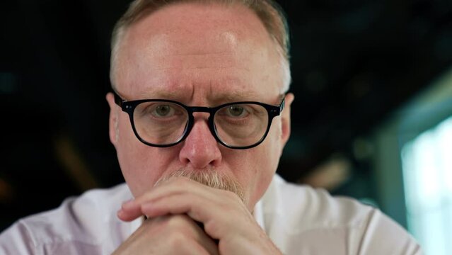 Focused strict serious face of a senior Caucasian man with fair hair in glasses. Portrait of a tired pensive businessman taking off his glasses thinking hard. Close up.