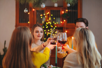 Happy young friends clinking glasses of wine over table decorated for Christmas celebration
