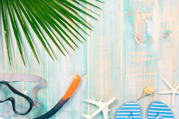 Top view composition on worn turquoise wooden background with palm leaf, diving goggles, snorkel...