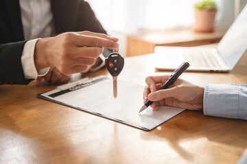Naklejka premium Business car rental company service, Close up hand of agent dealer giving, holding car key to customer renter, new owner after signed rental, purchase contract in document, vehicle sales agreement.