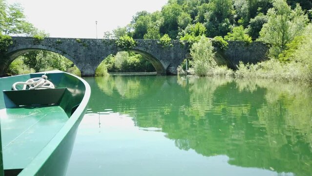 A boat floats along the river on a sunny day passing under an ancient stone bridge, view from the boat