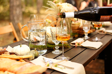Glass of orange wine placed near dishware and bouquet of fresh flowers amidst assorted fruits on...