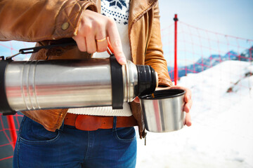 Young woman holding thermos on mountain top in winter - obrazy, fototapety, plakaty