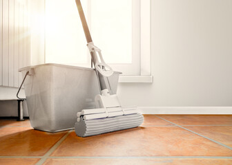 A mop and bucket are on the kitchen floor, wet cleaning.