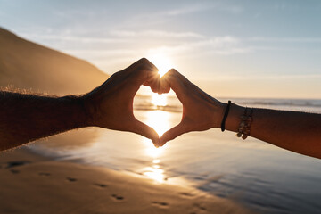 Two hands forming a heart shape against a vibrant sunset sky Symbolizing love Charity and unity...