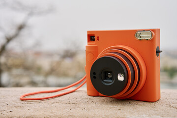 Vintage Orange Instant Camera in city with cloudy sky. Travel shooting equipment