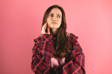 Fototapeta premium Portrait of minded brunette woman touch hand chin look at side think thoughts plan wear plaid shirt, long sleeves isolated over pink color background.