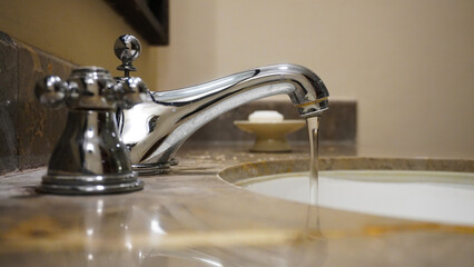 Selective focus draining water from stainless chrome faucet with hand soap bar                     ...