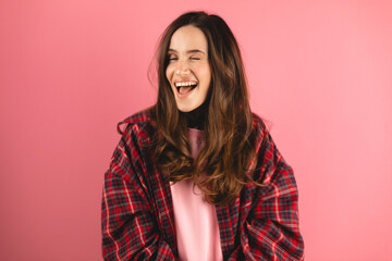 Playful happy contented brunette woman wear plaid shirt blinking eye, looking at camera with toothy smile, winking and flirting, expressing optimism. Indoor studio shot isolated on pink background. - obrazy, fototapety, plakaty