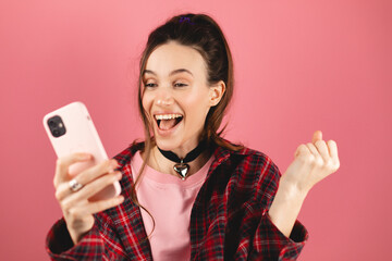 Amazed brunette woman with high ponytail look surprised wow on pink background. Girl look on mobile...