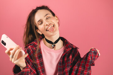 Amazed brunette woman with high ponytail look surprised wow on pink background. Girl look on mobile...