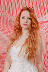 Red-haired princess in a white festive dress and a crown with emeralds on a red background with nets - 784671144