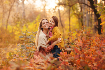Young beautiful mother hugs her little smiling daughter outside in autumn forest