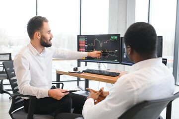 Two successful trader sitting in office, checking cryptocurrency information data on finance market...