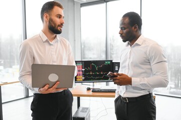 Fototapeta na wymiar Two diverse crypto traders brokers stock exchange market investors discussing trading charts research reports growth using pc computer looking at screen analyzing invest strategy, financial risks