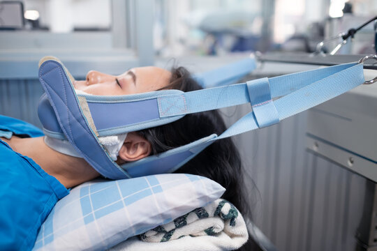female patient under cervical traction machine pulling the head for neck pain and treatment, physical therapist healthcare medical care. Laying down on the hospital bed with wires.