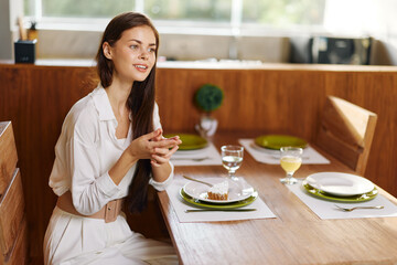 Elegant Woman Enjoying Romantic Dinner at Home A beautiful brunette woman sits at a stylishly set dining table, smiling ecstatically as she indulges in a homemade meal The table is adorned with a