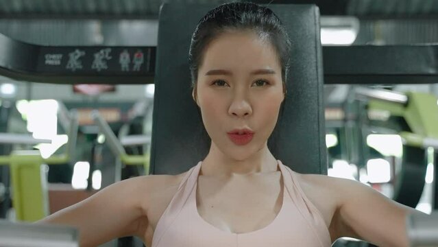 asian beautiful woman who using simulator for raising and spreading hands for pumping group of muscles in gym
