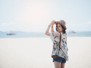 The concept of summer vacation at the beach. Happy Asian woman wearing a hat relaxing at the seaside and looking out in the summer against the backdrop of a cruise ship and a sea beach.