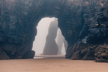 Playa de Las Catedrales in foggy day. Catedrais beach in Ribadeo, Lugo, Galicia, Spain. Natural archs of Cathedrals beach. Moody rock formations on misty day. Travel destination - 784680309