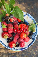 Raspberries, strawberry and wild blackberries on a vintage plate