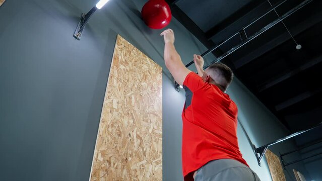 Functional training in gym. Man combined throwing of medicine ball and squats. Intense workout for endurance. Athlete in red shirt doing cross training. 4K, UHD