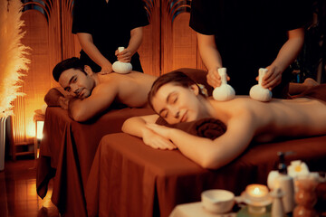 Hot herbal ball spa massage body treatment, masseur gently compresses herb bag on couple customer...