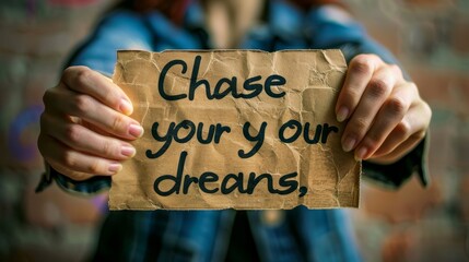 Close-up shot of a persons hands holding a handwritten sign that reads Chase your dreams
