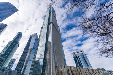 A tall skyscraper stands out among other towering buildings in a crowded urban landscape. The...