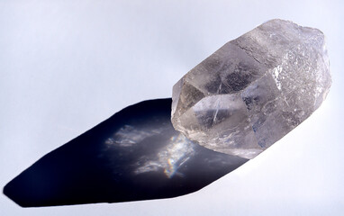 Translucent quartz mineral casts a black and white shadow on a white background