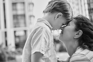 Fototapeta premium Adorable mother and son smiling happy having fun at city background. Motherhood concept, hugging. Boy 8 years old with mother in bright clothes enjoying summer day. High quality photo