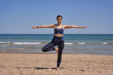 Healthy woman in sportswear doing yoga on the beach