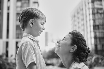 Adorable mother and son smiling happy having fun at city background. Motherhood concept, hugging. Boy 8 years old with mother in bright clothes enjoying summer day. High quality photo