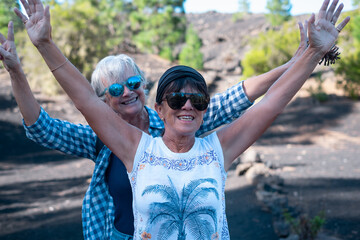 Happy couple of senior females with outstretched arms walking outdoors in mountain enjoying nature...