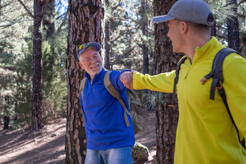 A happy grandfather and grandson couple hike on outdoor excursion together in the pine forest of...
