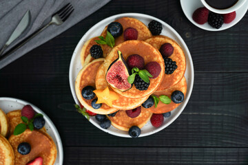 A flatlay of golden pancakes on a black wooden background,  topped with fresh berries create a cozy and indulgent scene.