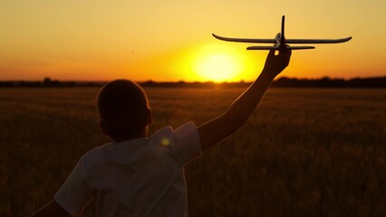 Child play with toy airplane. Happy boy runs with toy plane across field, flying into future. Kid...