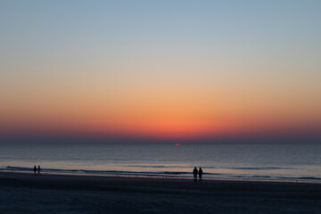 Figures in silhouette watch the sun rise over the ocean, very early morning beach walkers,...