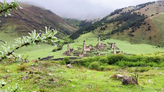 View of the medieval Targim tower complex in the Caucasus mountains surrounded by greenery. The Caucasus Mountains on a cloudy day in Ingushetia. Russia, 4K.