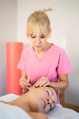 Professional beautician applying ear probe on female client in salon during auriculotherapy - 784714368