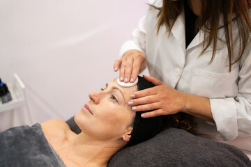 Crop beautician using skin care cotton pad on face of client in beauty salon