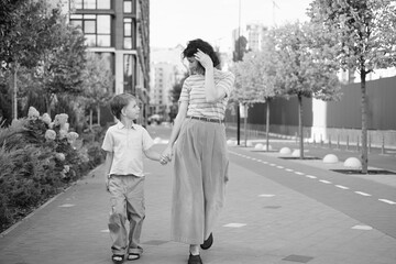 Caucasian young beautiful happy mother and cute small son walking the street and looking at each other. Woman and little boy smiling, talking and having vacations. High quality photo