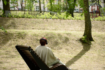 A woman in the park sits on a bench and listens to music. Millennium Park,  Zielona Gora, Poland 2024.