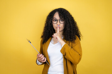 African american business woman with paperwork in hands over yellow background asking to be quiet with finger on lips. Silence and secret concept.