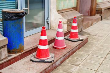 Three red and white traffic cones on building steps